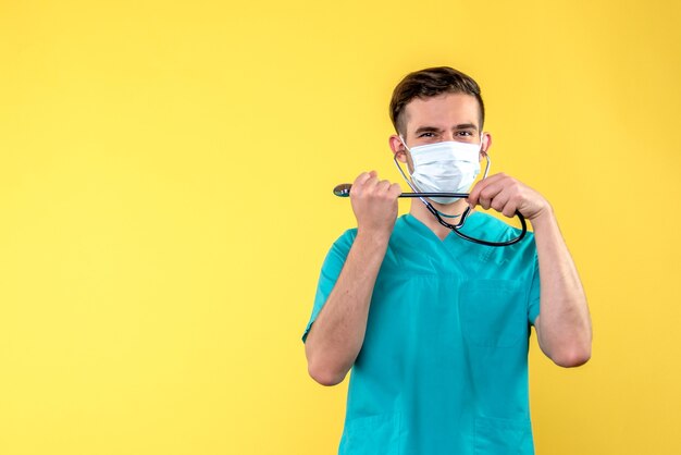 Front view of male doctor with stethoscope and mask on yellow wall