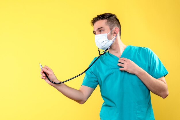 Front view of male doctor with stethoscope and mask on yellow wall