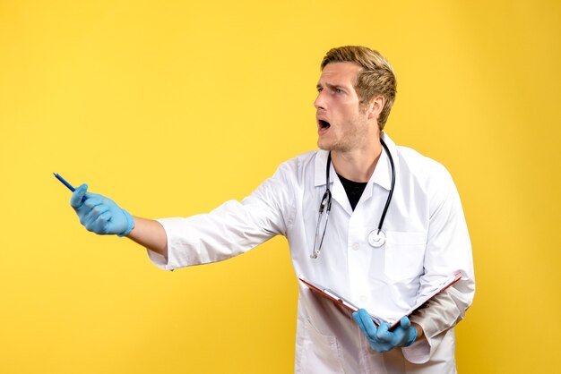 Front view male doctor writing notes on a yellow background virus health medic human