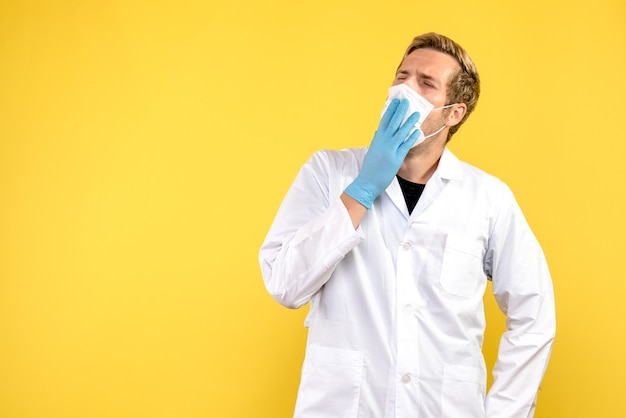 Вид спереди мужчина-врач, зевая в маске на желтом фоне, пандемия здоровья covid- medic