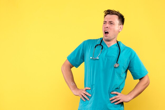 黄色の壁にあくびをする男性医師の正面図