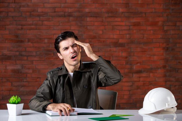 Front view male engineer sitting behind his working place and having headache job agenda document contractor corporate property builder plan business