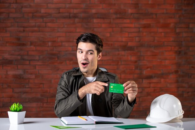 front view male engineer sitting behind his working place and holding credit card builder agenda property contractor money job corporate business