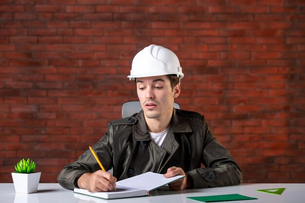 흰색 헬멧 쓰기 메모 문서 계획 비즈니스 속성 작업 의제 빌더 기업에 그의 작업 장소 뒤에 앉아 전면보기 남성 엔지니어