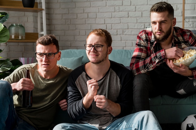 Front view of male friends watching sports on tv and having beer and snacks