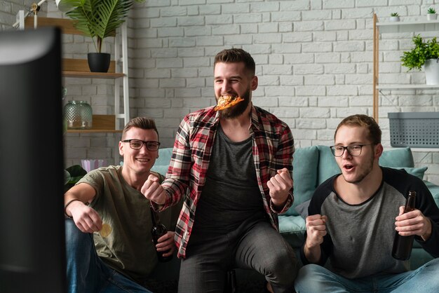 Front view of male friends watching sports on tv and having pizza