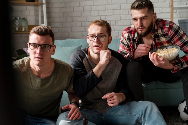 Free photo front view of male friends watching sports on tv and having snacks