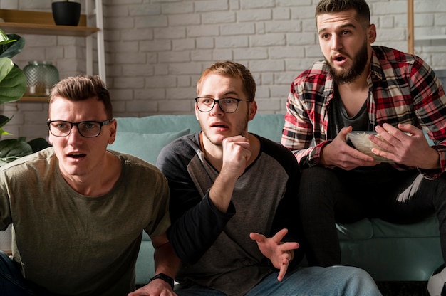 Front view of male friends watching sports on tv together and having snacks