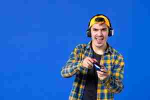 Free photo front view of male gamer with gamepad and headphones playing video game on blue wall