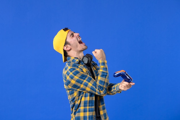 青い壁でビデオゲームをプレイするゲームパッドを持つ男性ゲーマーの正面図