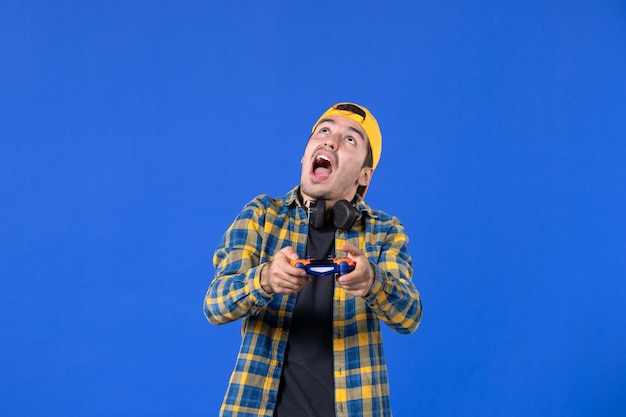 Front view of male gamer with gamepad playing video game on blue wall