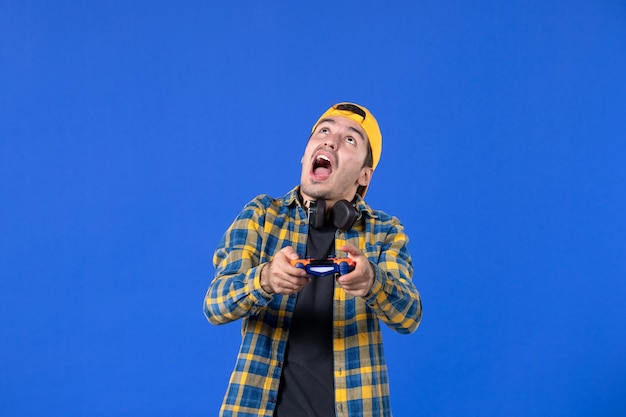 Вид спереди геймера-мужчины с геймпадом, играющего в видеоигру на синей стене