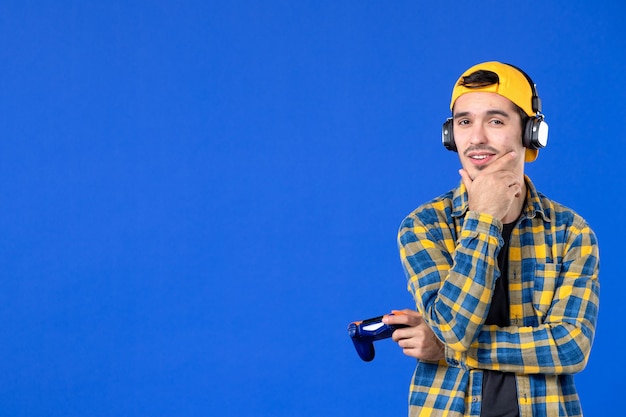 Front view of male gamer with gamepad playing video game on blue wall