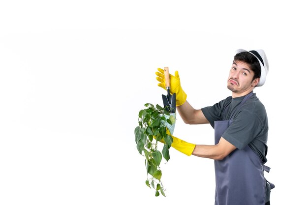 Садовник-мужчина, вид спереди, держит маленькое растение в горшке и шпатель на белом фоне