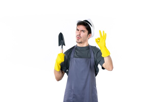 Front view male gardener in yellow gloves holding little spatula on the white background flower tree job garden color ground grass work bush