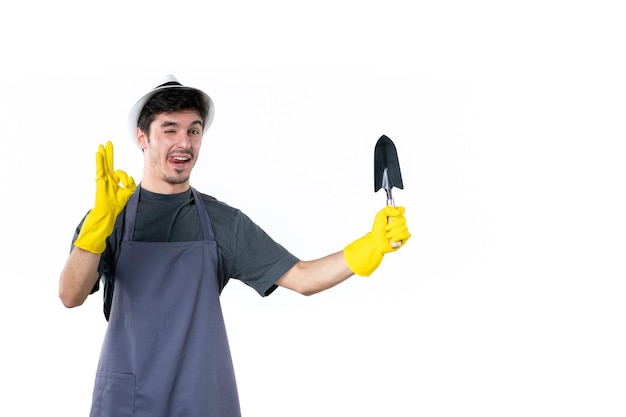 Front view male gardener in yellow gloves holding little spatula on white background ground tree flower work bush job color garden