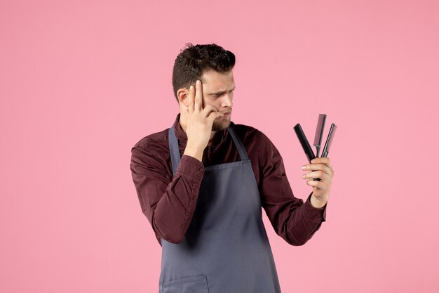 front view male hairdresser holding hairbrushes on pink background