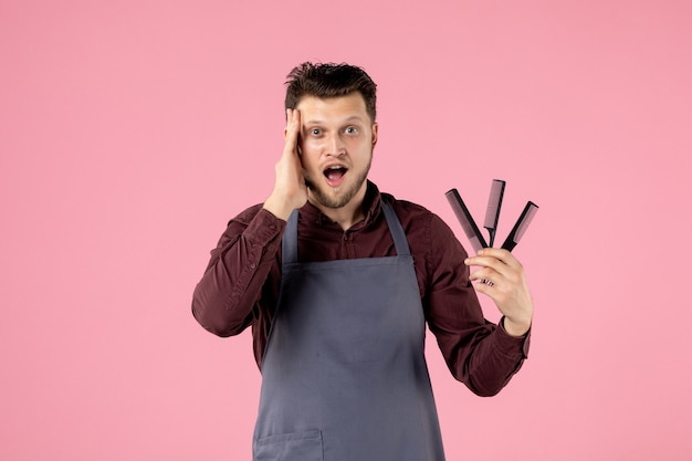 front view male hairdresser holding hairbrushes on pink background