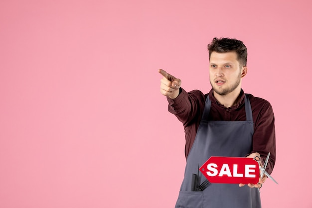 Free photo front view male hairdresser with red sale nameplate on pink background