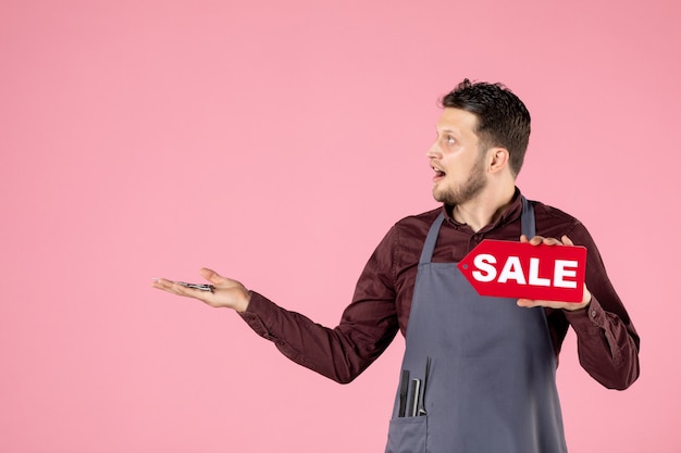 Бесплатное фото Мужской парикмахер вид спереди с табличкой продажи и ножницами на розовом фоне