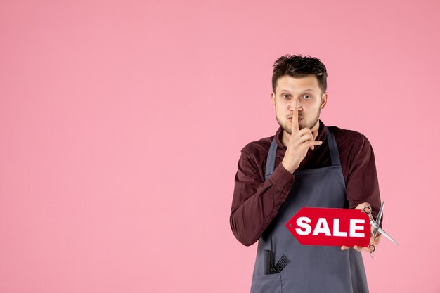 front view male hairdresser with sale nameplate and scissors on pink background