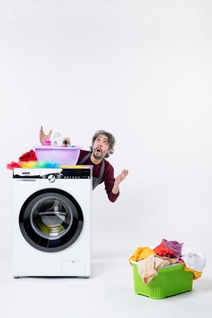 Front view male housekeeper looking up sitting behind washer laundry basket on white wall