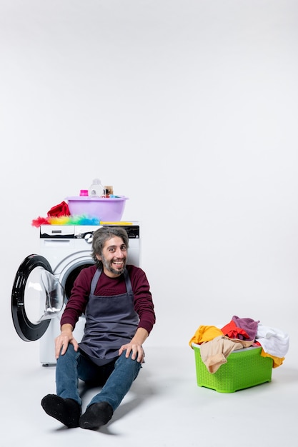 Front view male housekeeper sitting in front of washer laundry basket on white wall