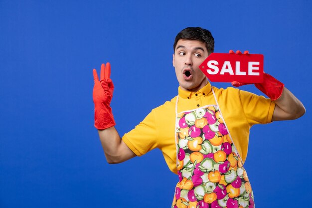 Вид спереди мужская домработница с красными сливными перчатками держит знак продажи, делая знак ОК на синем пространстве