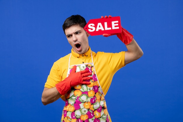 Governante maschio di vista frontale in maglietta gialla che mette il segno di vendita vicino alla sua testa su spazio blu