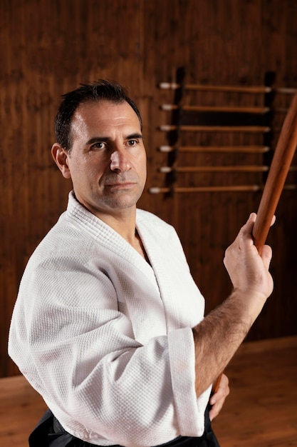 Вид спереди инструктора мужских боевых искусств в тренировочном зале с деревянной палкой