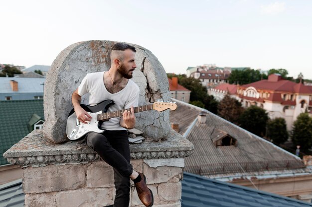 Front view of male musician on roof top playing electric guitar