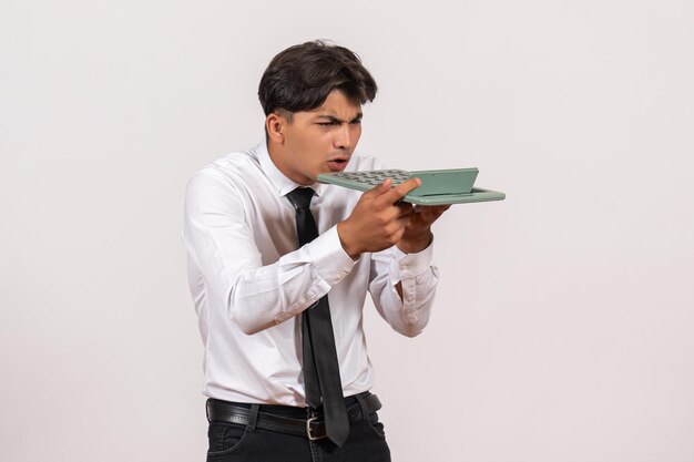 Front view male office worker holding calculator on white wall work office human job