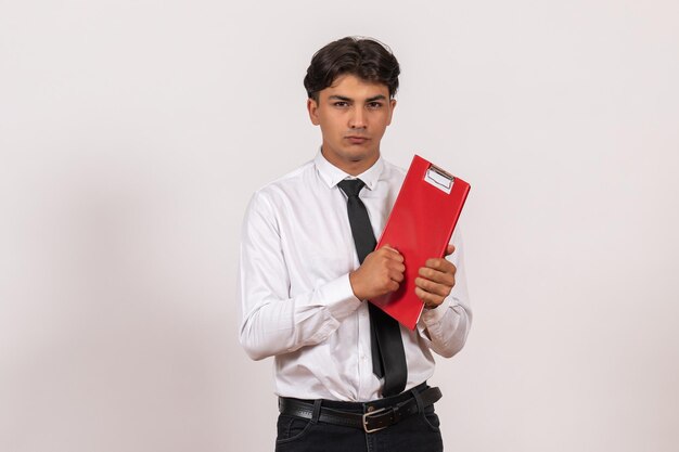 Вид спереди мужской офисный работник, держащий красный файл на белой стене, офисная работа, человеческая работа