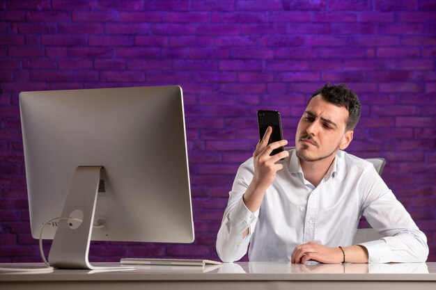 Front view male office worker sitting behind his working place talking