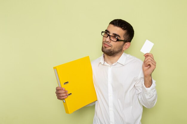 Front view of male office worker in white shirt holding card and files on green wall