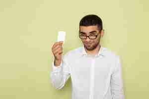 Free photo front view of male office worker in white shirt holding card with smile on the light-green wall