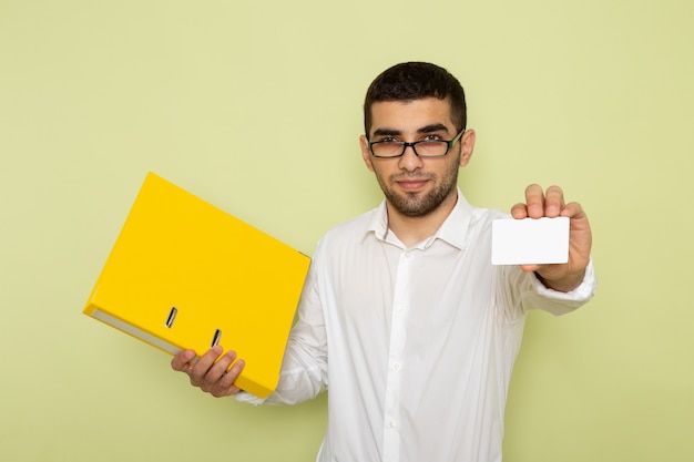 Front view of male office worker in white shirt holding card and yellow files on green wall