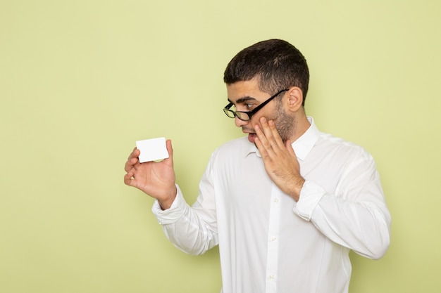 Front view of male office worker in white shirt holding plastic card on the light-green wall