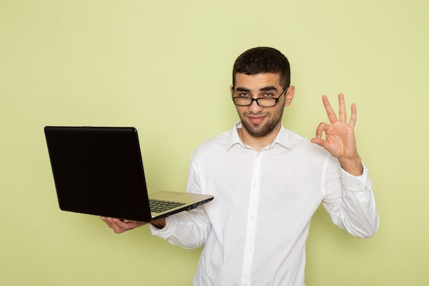 Front view of male office worker in white shirt holding and using laptop on green wall