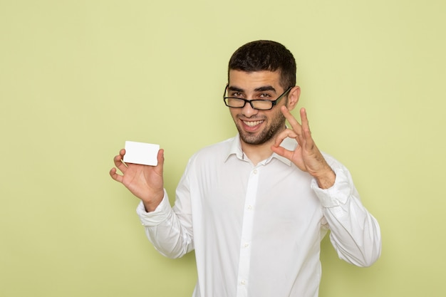 Вид спереди мужского офисного работника в белой рубашке, держащего белую карточку на светло-зеленой стене