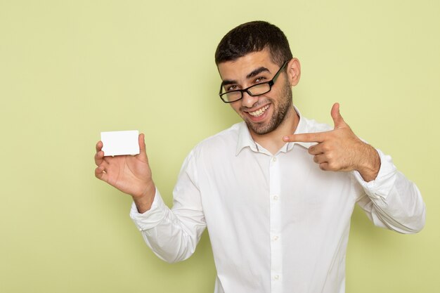 Front view of male office worker in white shirt holding white plastic card on light green wall