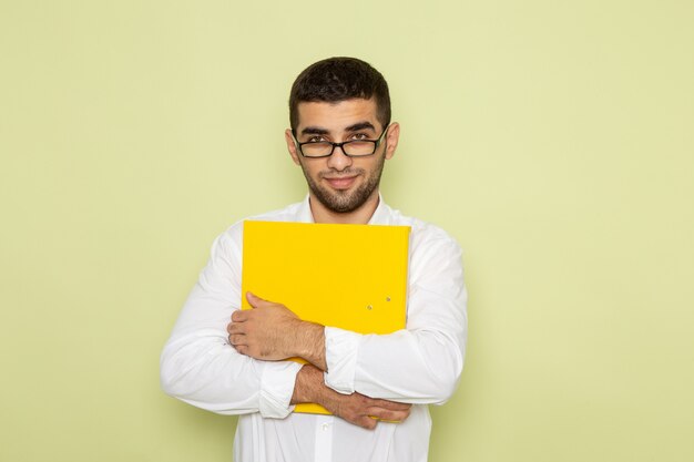 緑の壁に笑みを浮かべて黄色のファイルを保持している白いシャツの男性サラリーマンの正面図