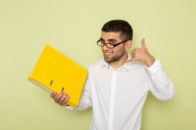 Front view of male office worker in white shirt holding yellow files smiling on the green wall