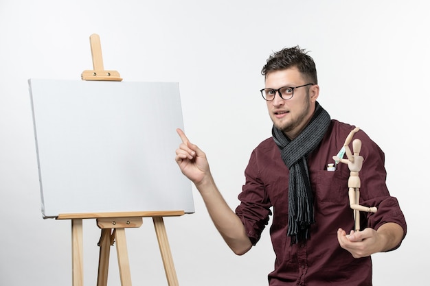 Front view male painter along with easel holding human figure on the white wall