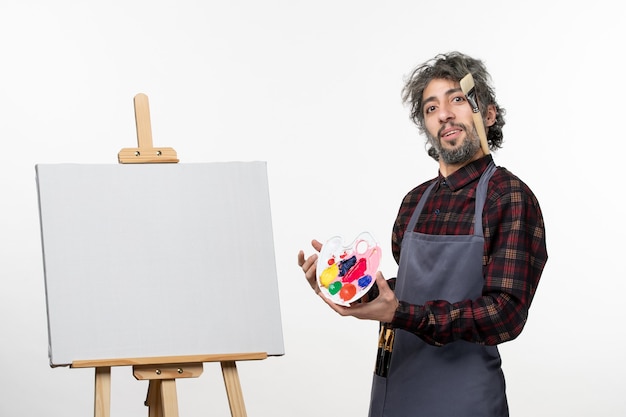 Бесплатное фото Художник-мужчина, вид спереди, держащий краски и готовящийся рисовать на белой стене