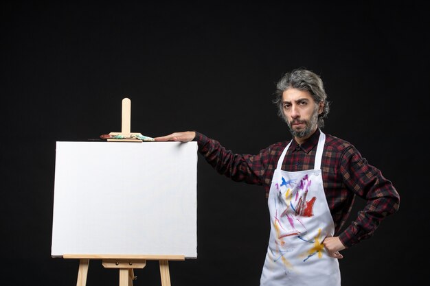 Front view of male painter with easel for drawing on black wall