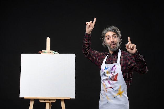 Front view of male painter with easel for drawing on black wall