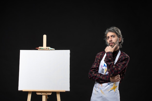 Front view of male painter with easel for drawing posing on black wall