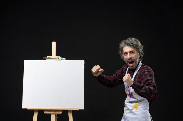 Front view of male painter with easel rejoicing on black wall