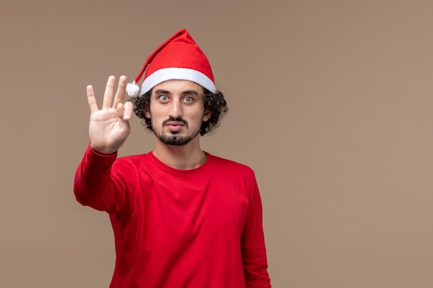 Вид спереди мужчина в красном, показывающий номер на коричневом фоне, праздник эмоции, рождество